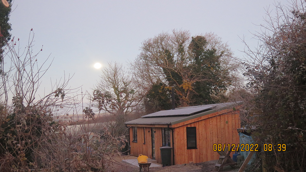 Early December and the moon sets over a completed wooden cabin.